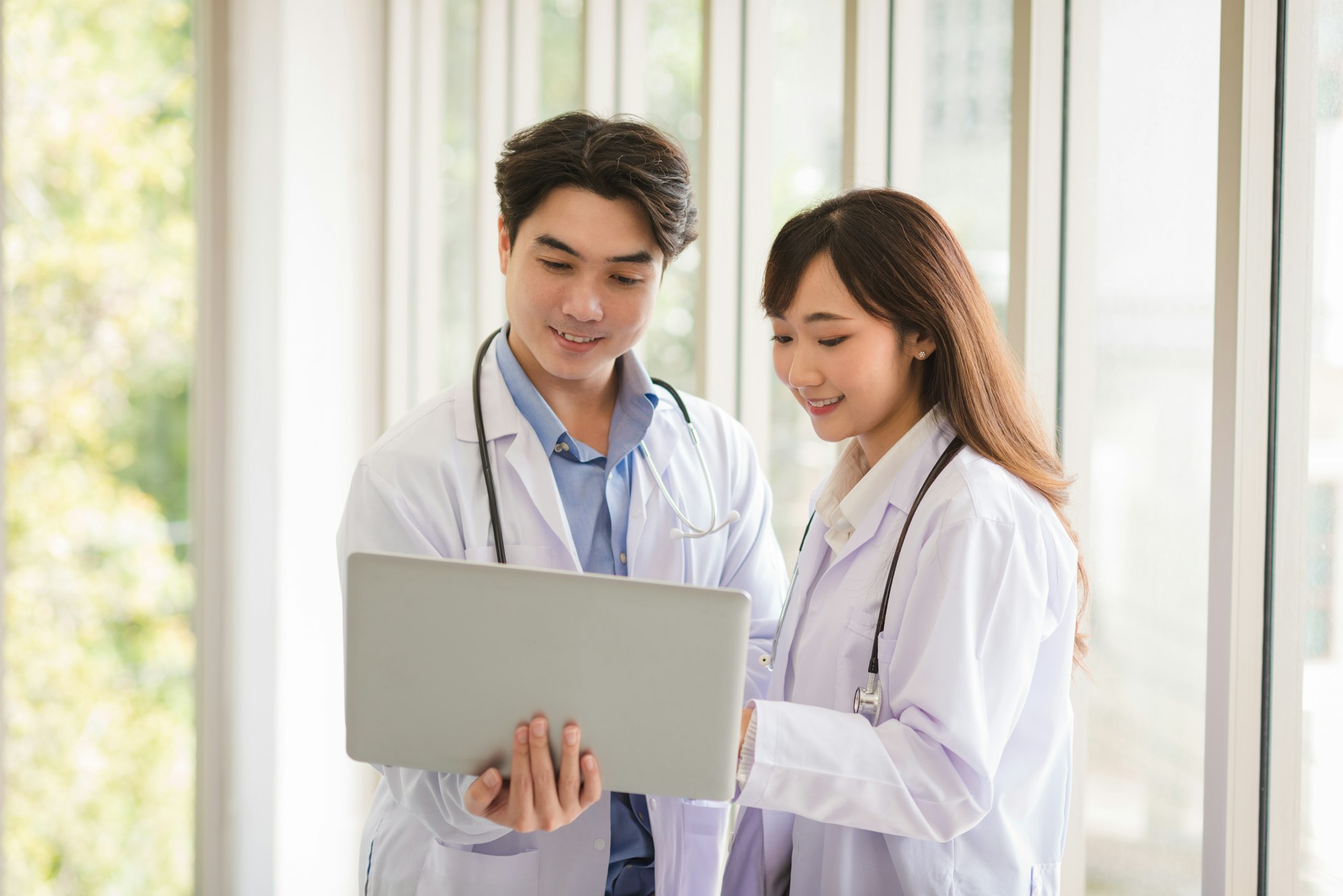 Group of Asian doctors team portrait standing and using laptop with other colleagues in background.